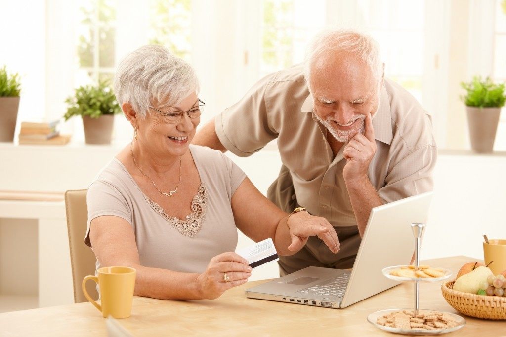 Happy older couple doing online shopping, laughing wife pointing
